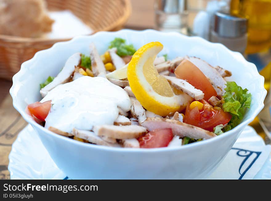 A bow of fresh chicken salad with vegetables and sauce on a table.