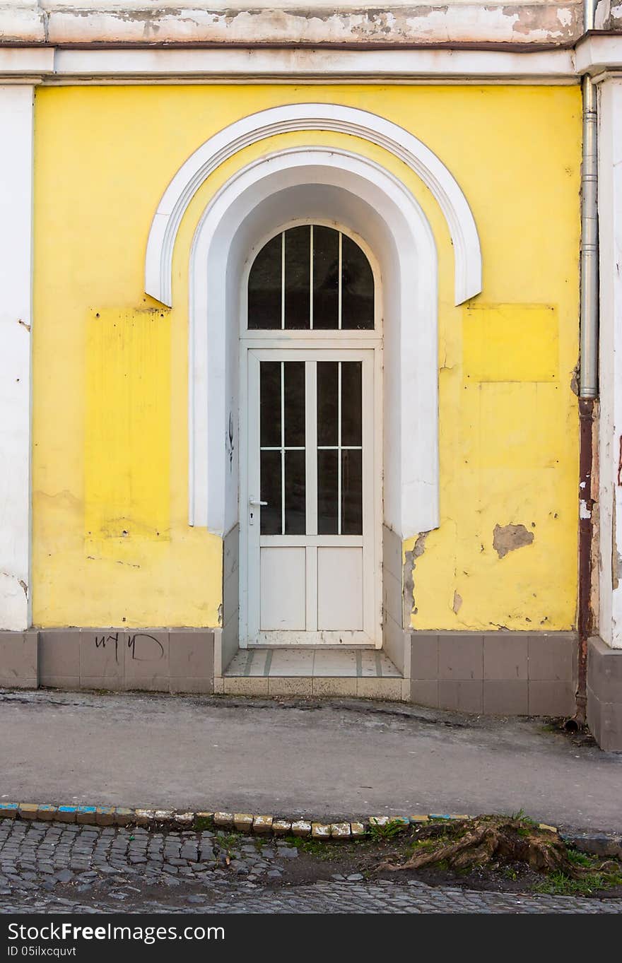 New plastic door inserted into the arched doorway of a building on the old cobbled street near the cutted tree. New plastic door inserted into the arched doorway of a building on the old cobbled street near the cutted tree