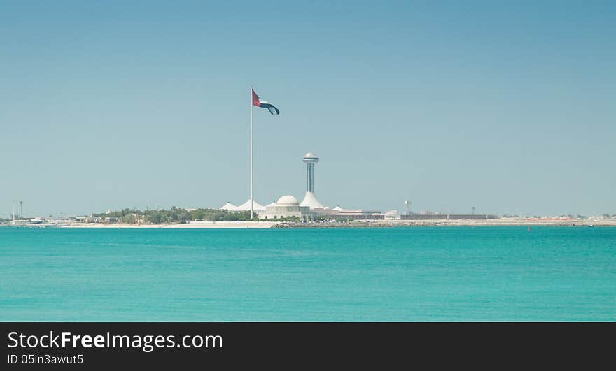 The United Arab Emirates flag, flying next to the Abu Dhabi Heritage Theatre with incredible turquoise water