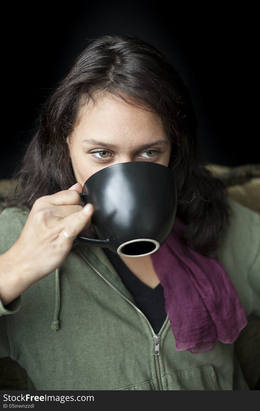 Portrait of a beautiful young woman with striking green eyes drinking coffee from a black cup. Portrait of a beautiful young woman with striking green eyes drinking coffee from a black cup.