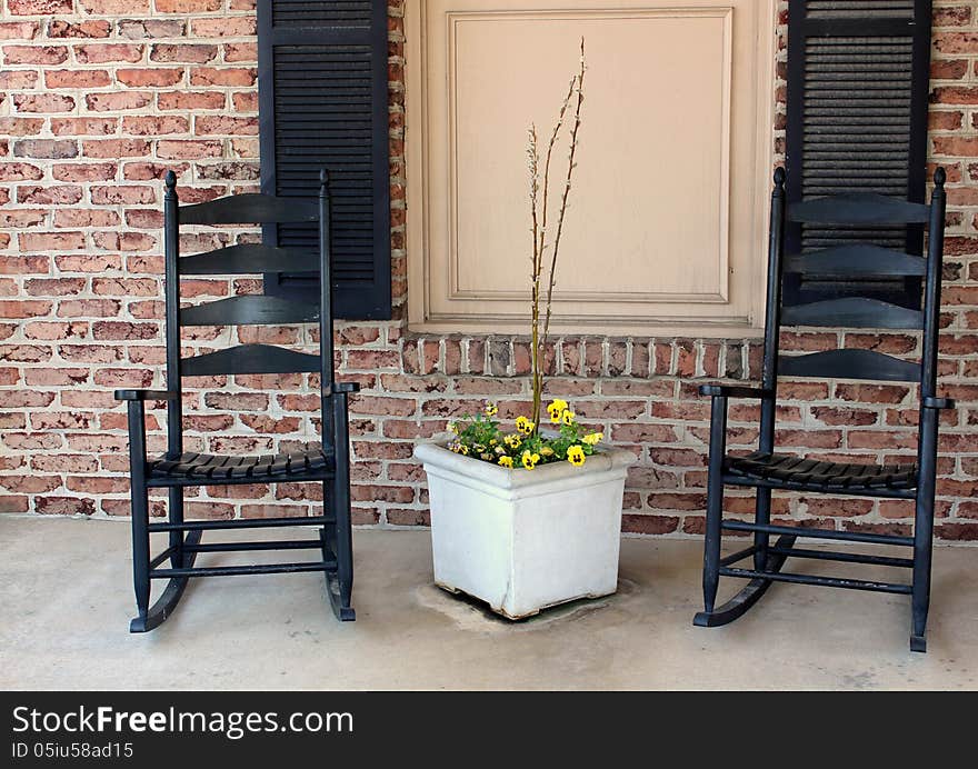 Two black rocking chairs set on a quiet brick porch,inviting people to sit for awhile and take a break from life's sometimes hectic pace. Two black rocking chairs set on a quiet brick porch,inviting people to sit for awhile and take a break from life's sometimes hectic pace.