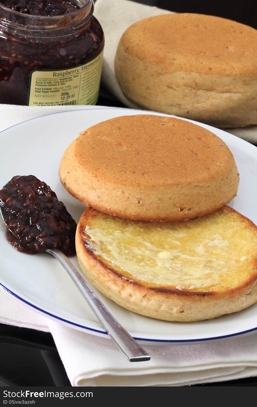 Toasted English muffins spread with butter and raspberry jam.