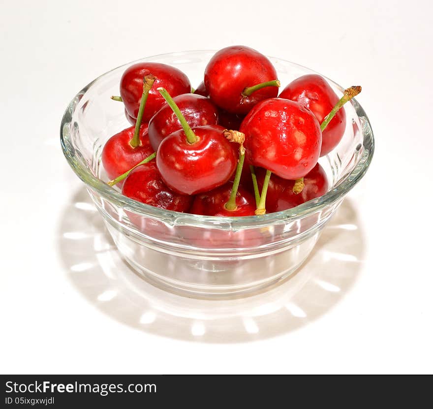 A glass bowl of cherries with a shadow.