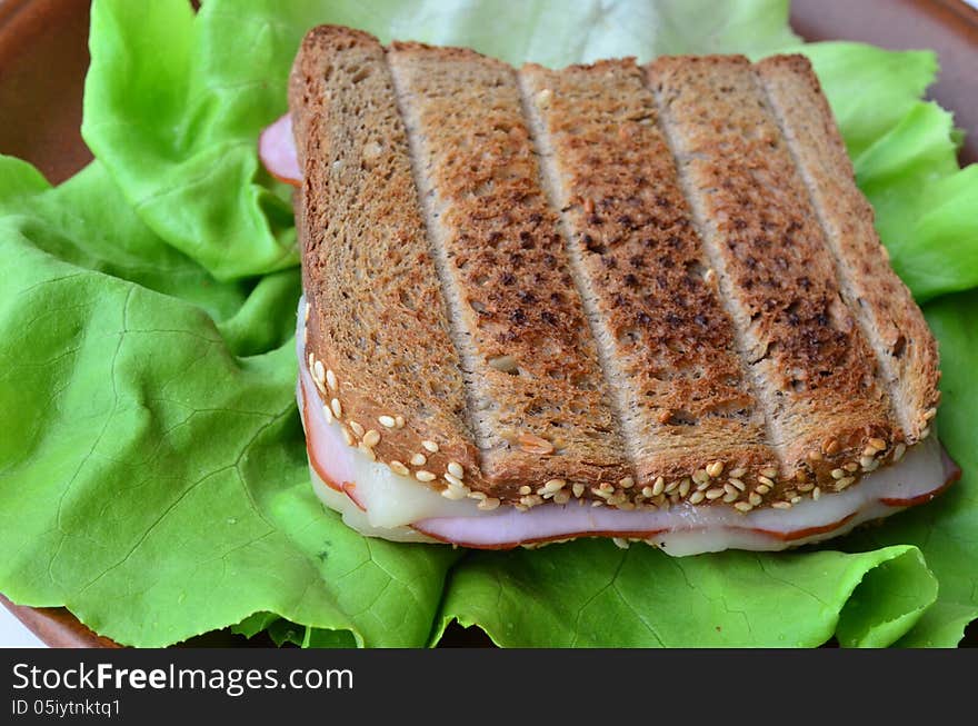 Integral toast with sesame and other whole seeds, ham and cheese sandwich served on a brown porcelain plate over fresh lettuce leaf, a cloaser look. Integral toast with sesame and other whole seeds, ham and cheese sandwich served on a brown porcelain plate over fresh lettuce leaf, a cloaser look