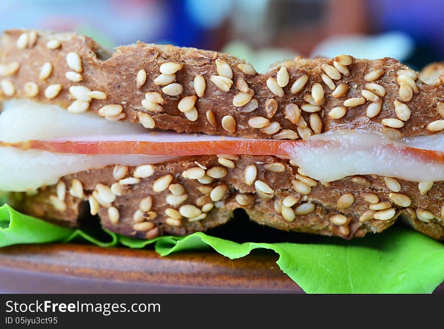 Integral toast with sesame and other whole seeds, ham and cheese sandwich served on a brown porcelain plate over fresh lettuce leaf, close up, side view. Integral toast with sesame and other whole seeds, ham and cheese sandwich served on a brown porcelain plate over fresh lettuce leaf, close up, side view