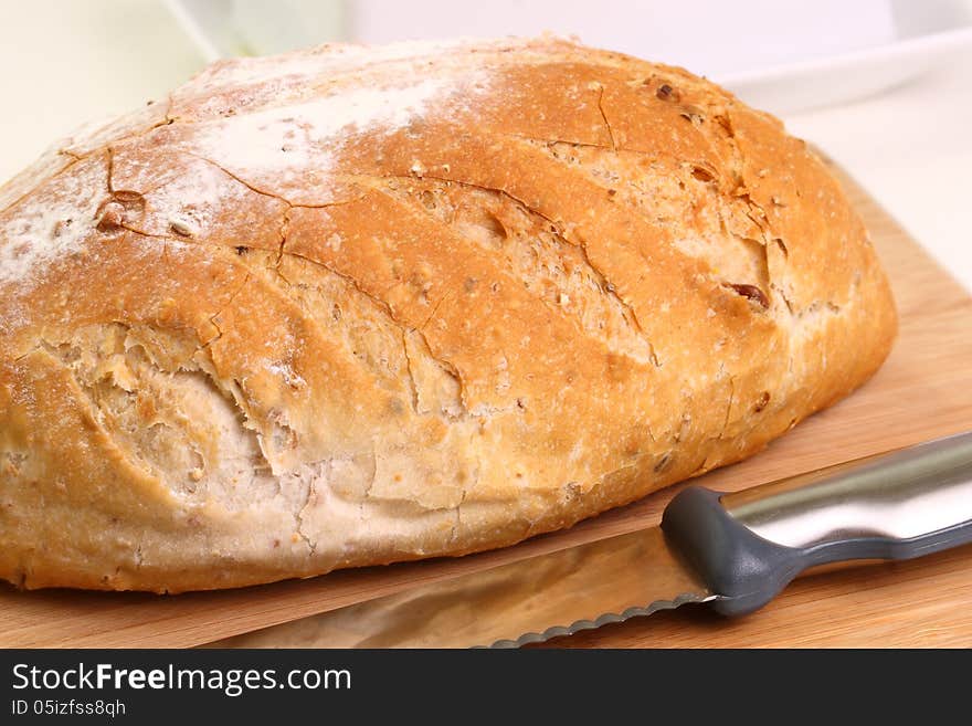 A sideview closeup of a crusty loaf of whole wheat bread on a cutting board ready for serving. A sideview closeup of a crusty loaf of whole wheat bread on a cutting board ready for serving.