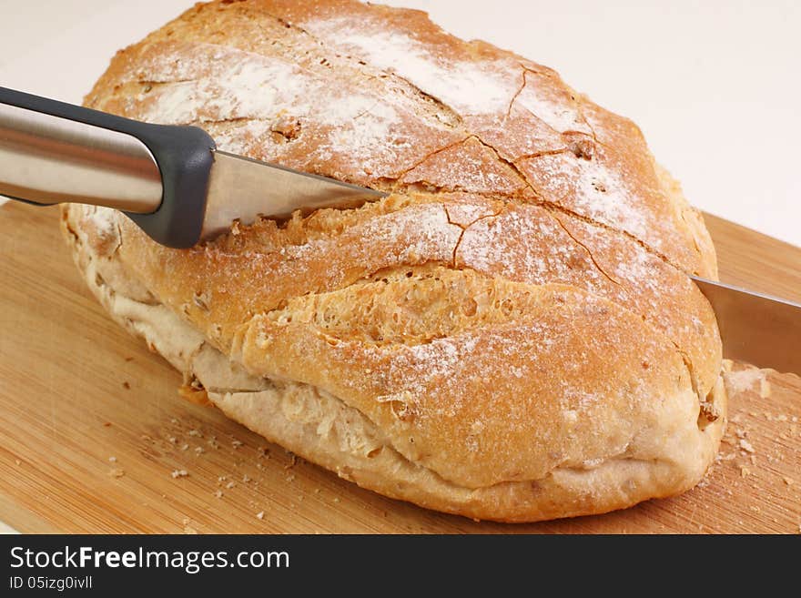 A loaf on a cutting board with a knife cutting into the bread. A loaf on a cutting board with a knife cutting into the bread.