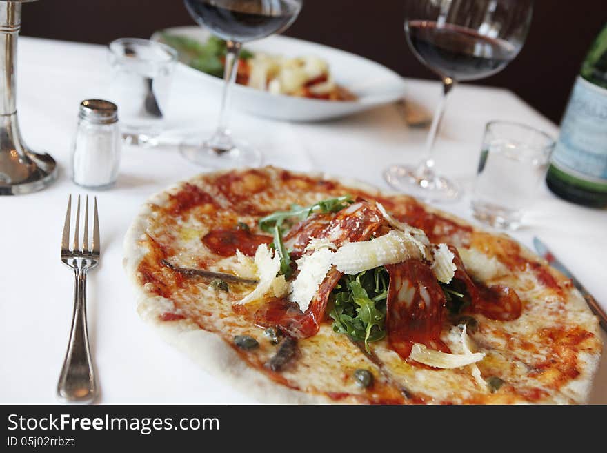 Covered table in the pizzeria, white tablecloth, sheen with red wine, pizza with fresh salad and beetle cheese