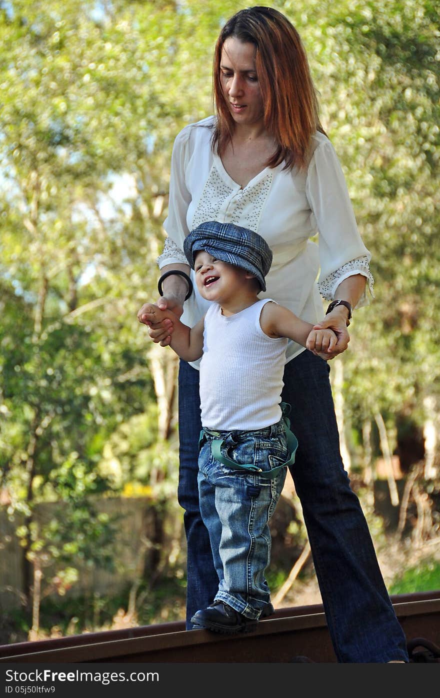 Young mother helping toddler baby boy to walk