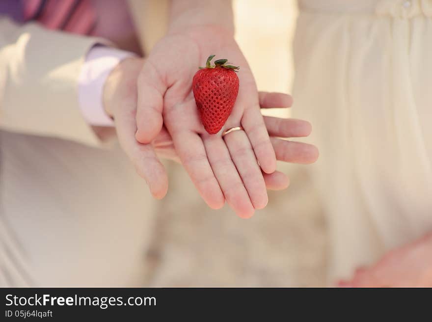 Close-up on hands of bride and groom is ripe strawberries