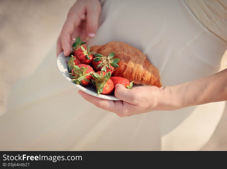 Woman's hands holding a white plate with strawberries and a croissant