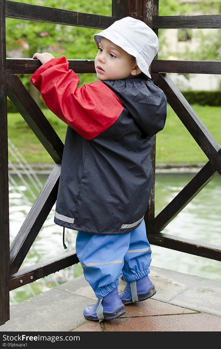 Child toddler in waterproof clothes in a park in rain. Child toddler in waterproof clothes in a park in rain.