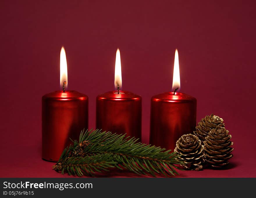 Burning red candles with twig of spruce