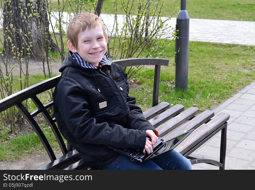 The teenager with the laptop sits on a bench in park