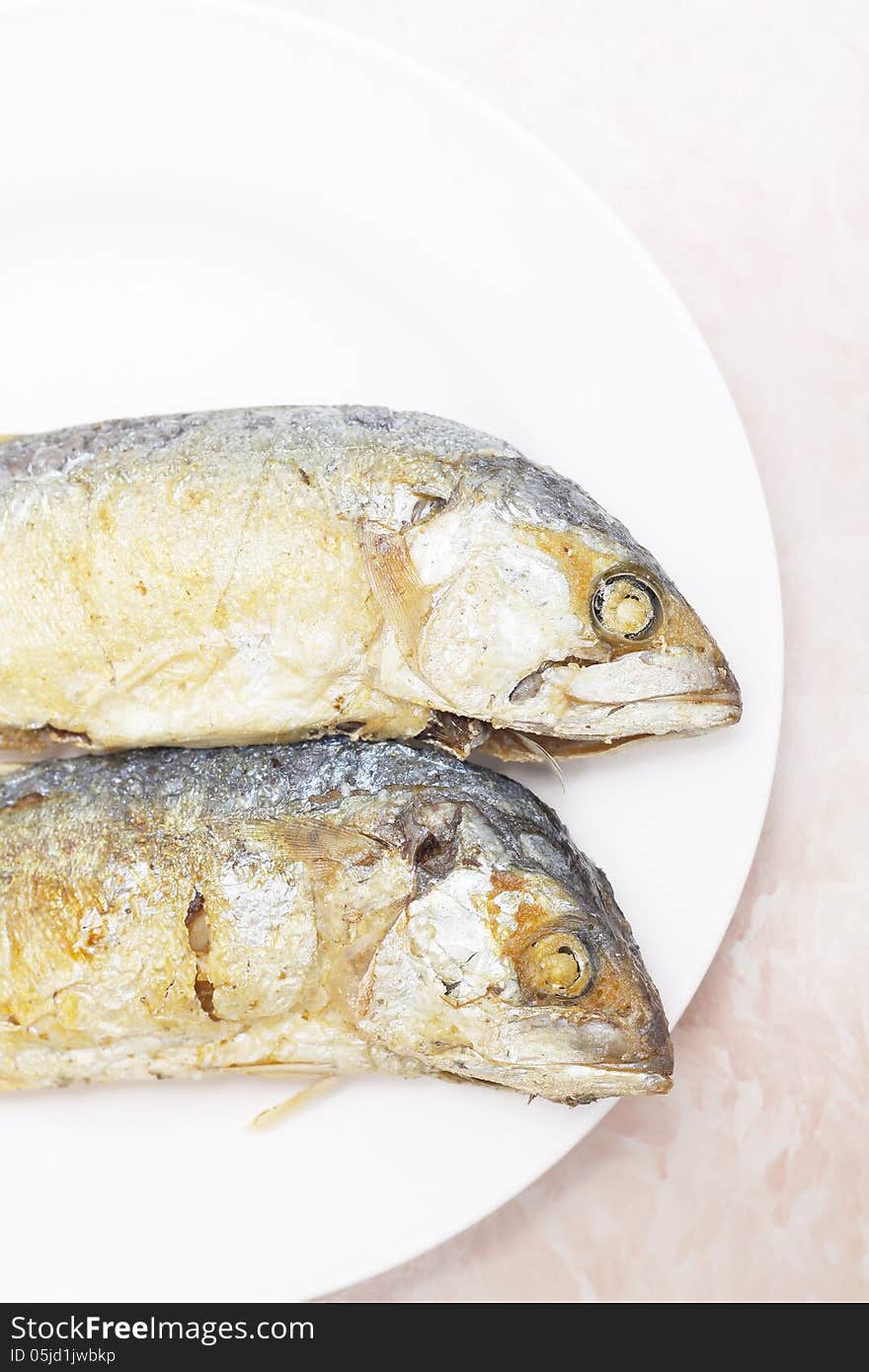 Two fried mackerel fishes on white plate