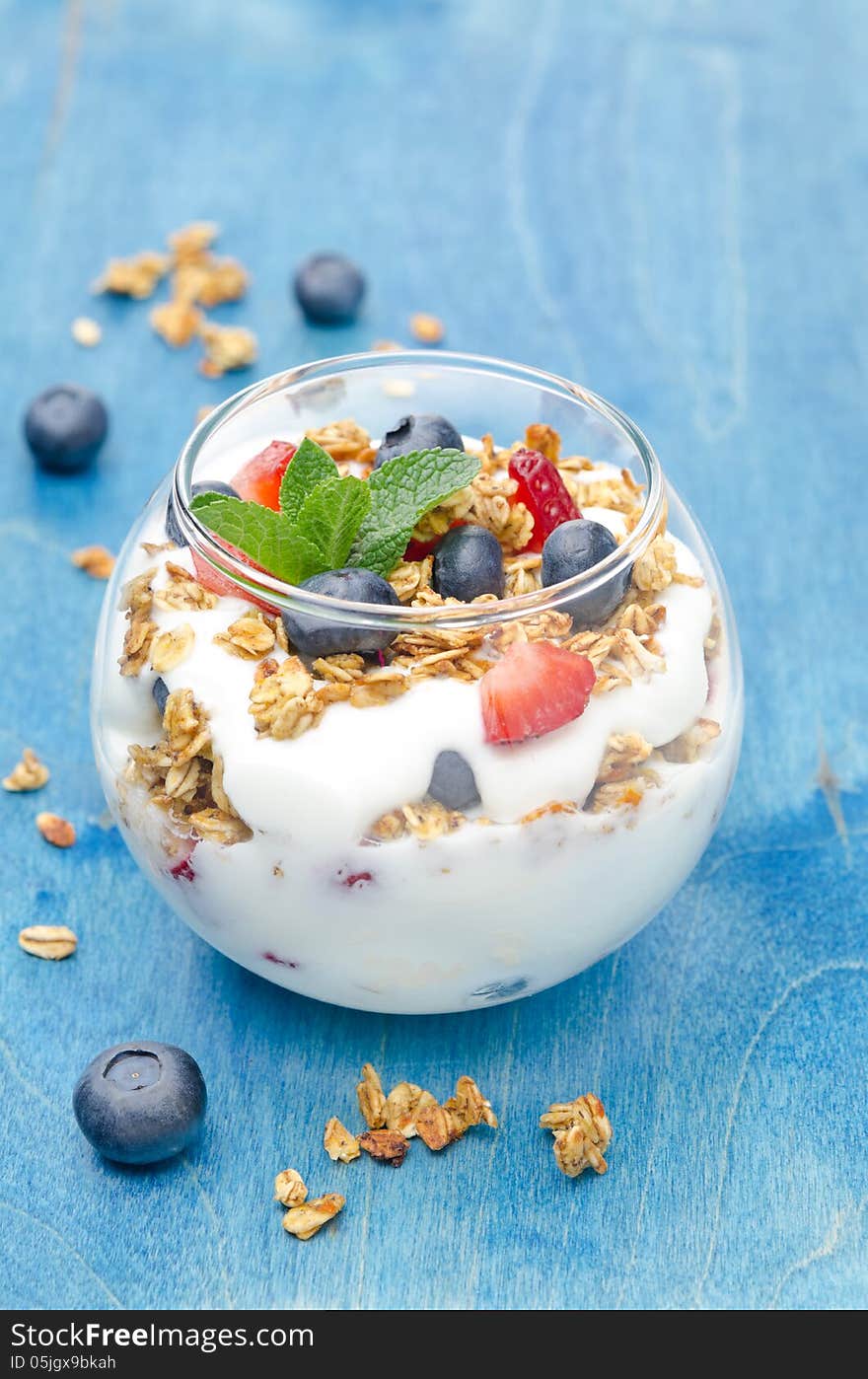 Layered dessert with yogurt, granola, fresh berries in a glass on a blue background