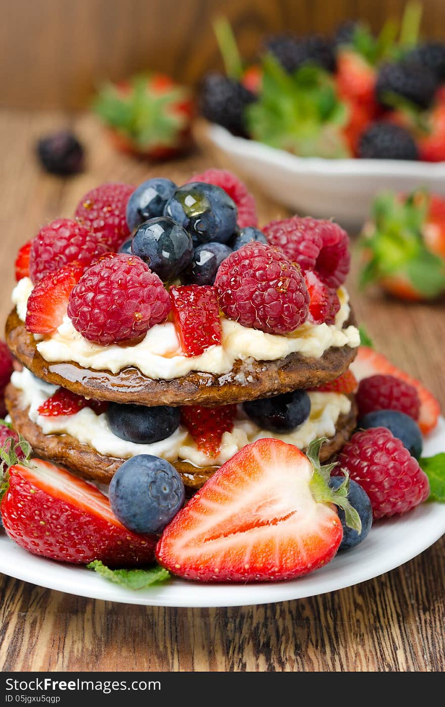 Pancake cake with whipped cream and fresh berries, bowl of berries in the background, close-up vertical