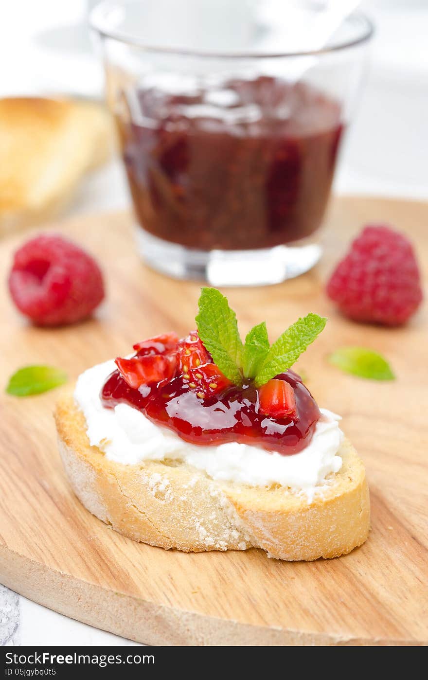 Piece of toasted baguette with cream cheese, raspberry jam and raspberries on a wooden board