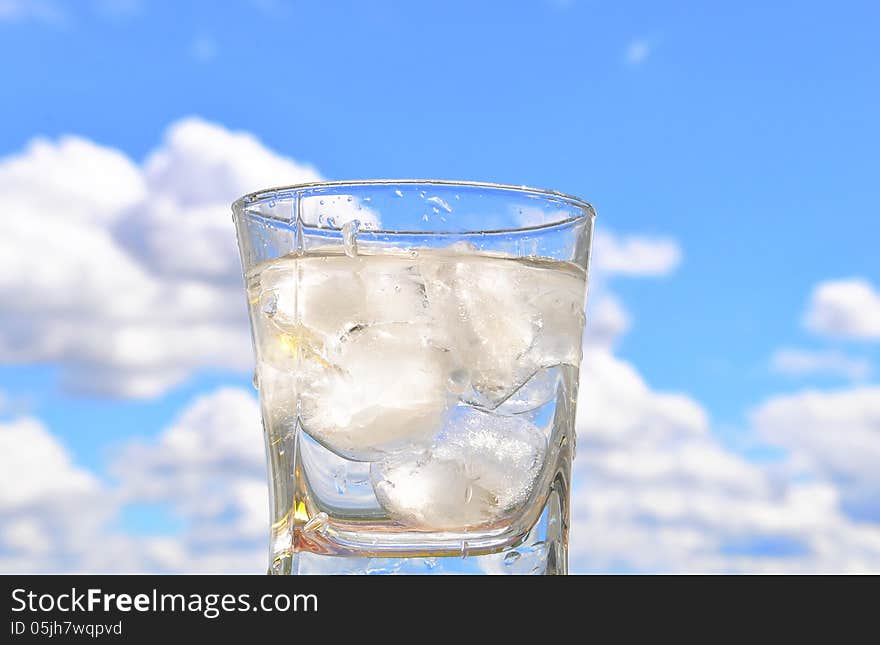 A glass glass of iced water on the background of blue sky. A glass glass of iced water on the background of blue sky