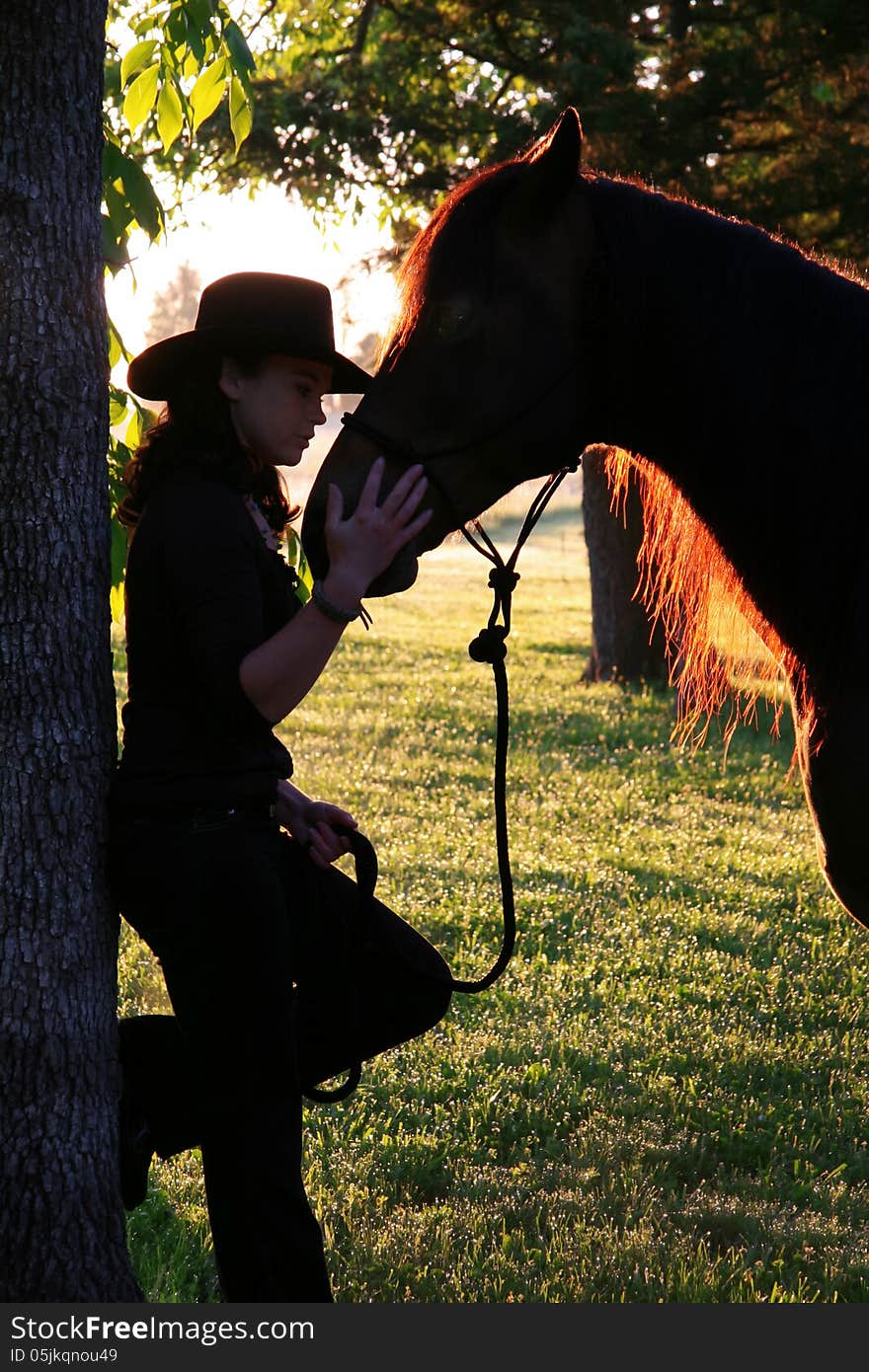 A cowgirl bonds with her horse at sunrise on the farm. A cowgirl bonds with her horse at sunrise on the farm