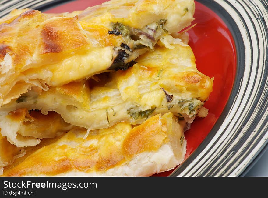 Slices of Cheese and Greens Puff Pastry Pie closeup on Red Plate. Slices of Cheese and Greens Puff Pastry Pie closeup on Red Plate