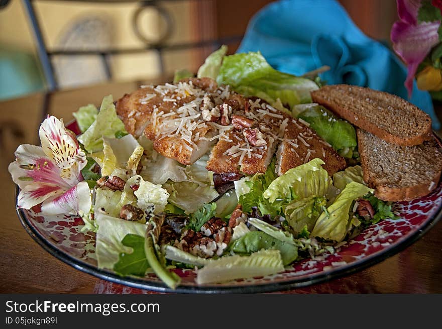 This is a chicken salad with flowers, nuts, and bread. with iceberg lettuce