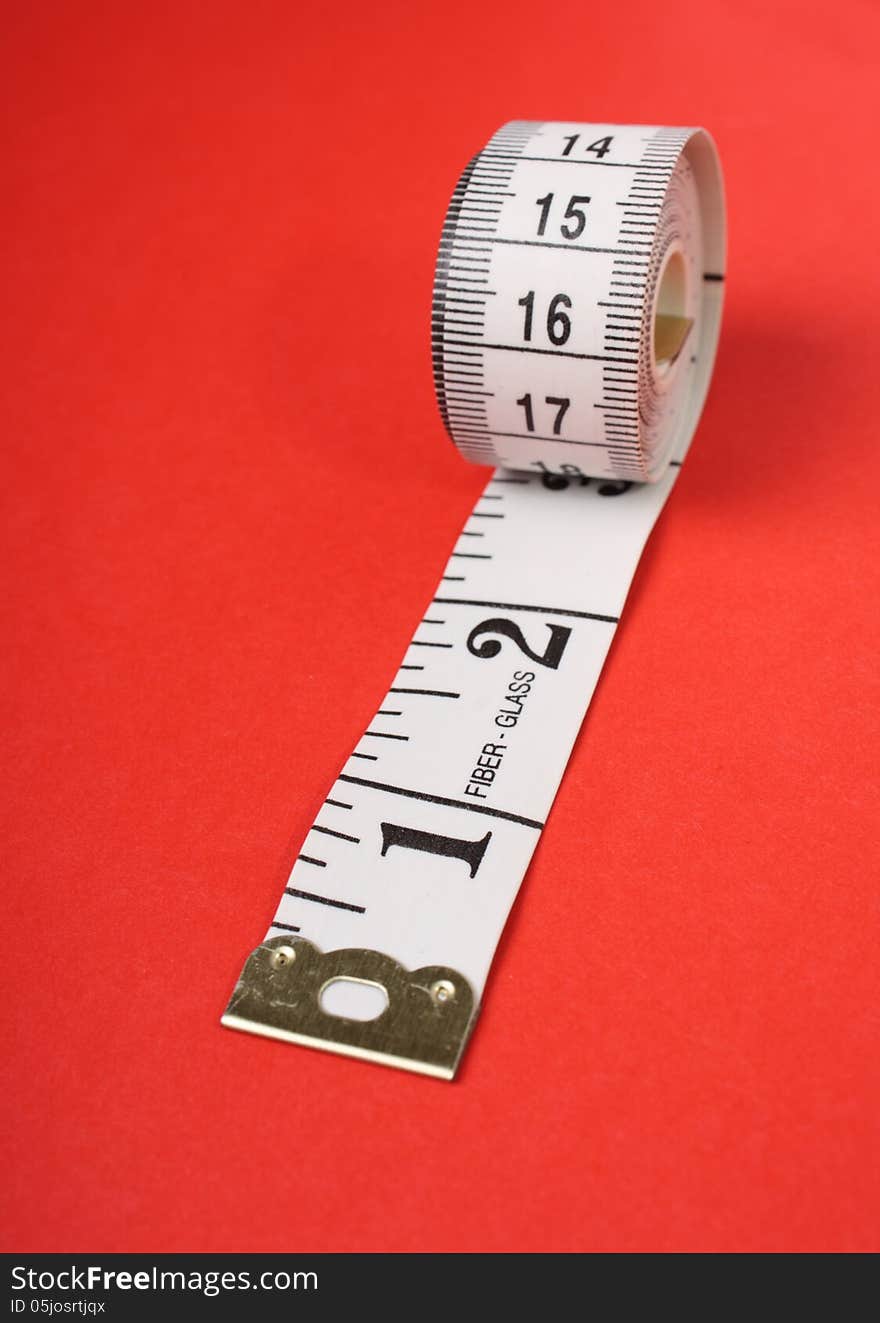 A rolled up white tape measure with both inches and centimetres on a red paper background