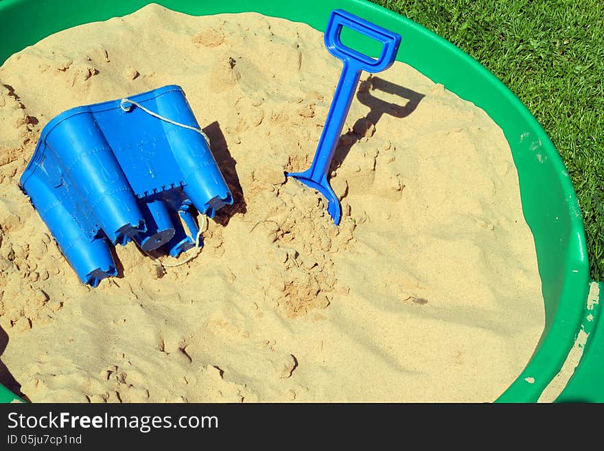 A childs sand pit with a bucket and spade in a garden on the grass. A childs sand pit with a bucket and spade in a garden on the grass.