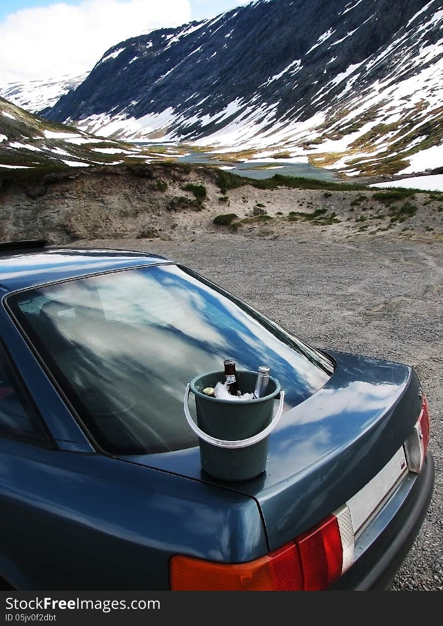 Beer bottle in the bucket with ice standing on the hood of the car