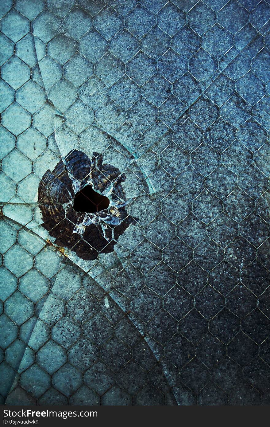 A cracked and broken blue-tinted window with what looks like a bullet hole. A cracked and broken blue-tinted window with what looks like a bullet hole