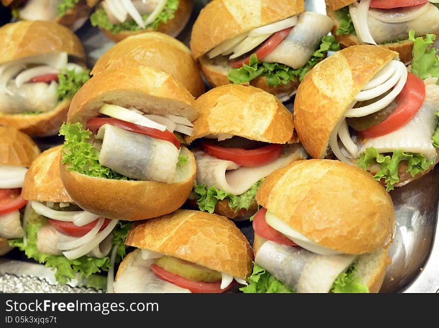 Closeup image of fresh and delicious seafood rolls stacked. The bread is filled with fresh raw fish and decorated with green salad, onions and tomatos. Closeup image of fresh and delicious seafood rolls stacked. The bread is filled with fresh raw fish and decorated with green salad, onions and tomatos.