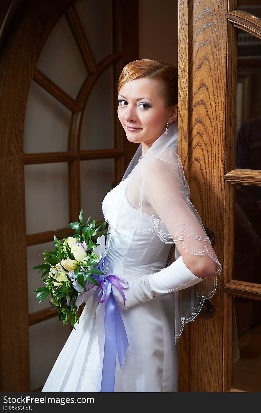 Happy beautiful bride with bouquet near doors