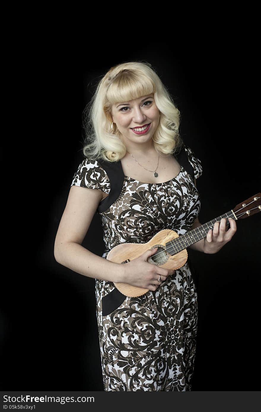 Portrait of a beautiful young woman with blond hair and brown eyes shot on a black background and playing a ukulele. Portrait of a beautiful young woman with blond hair and brown eyes shot on a black background and playing a ukulele.