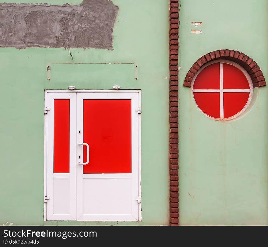 Red round window and a red door on a green old wall with bricks. Red round window and a red door on a green old wall with bricks