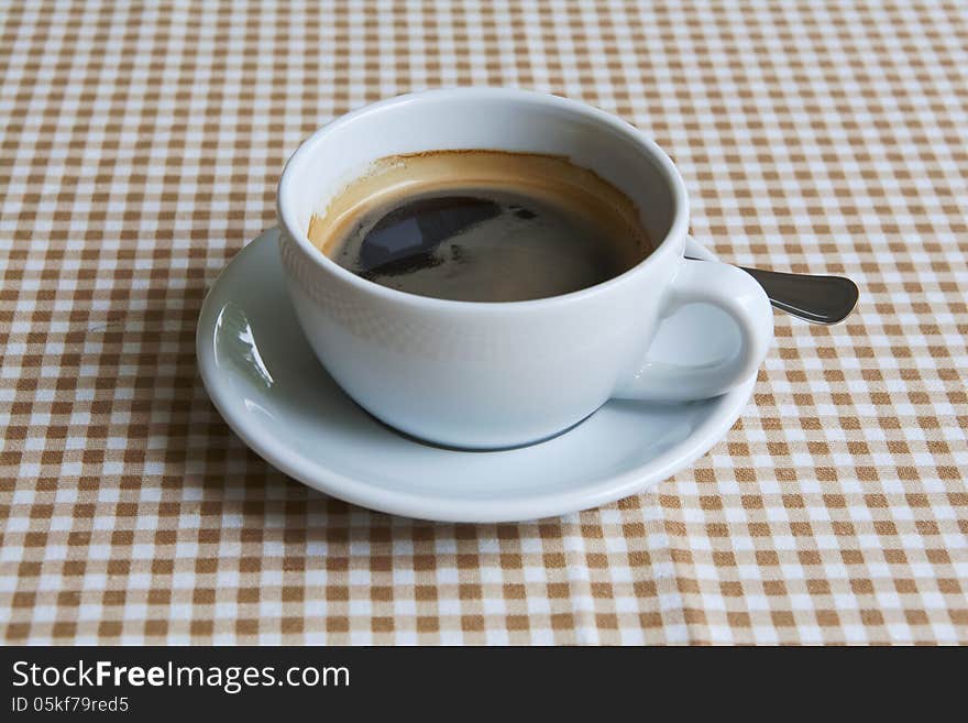 Cup of black coffee on table dressed with tablecloth