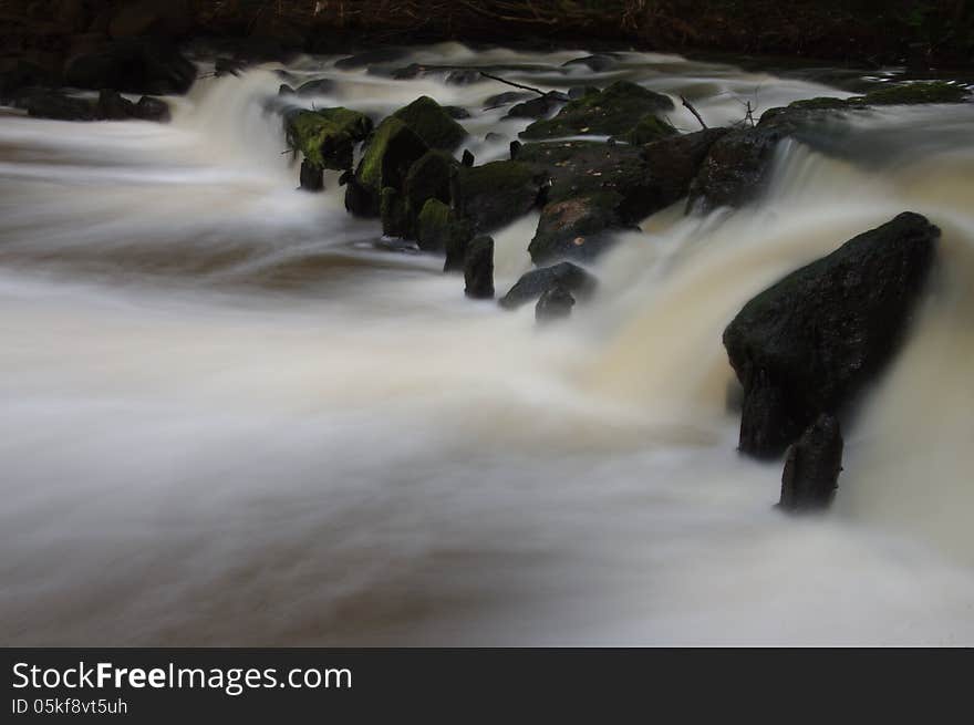 The photograph shows foamy waterfall on a small river. Due to the long exposure time of the effect of freezing water was obtained. The photograph shows foamy waterfall on a small river. Due to the long exposure time of the effect of freezing water was obtained.