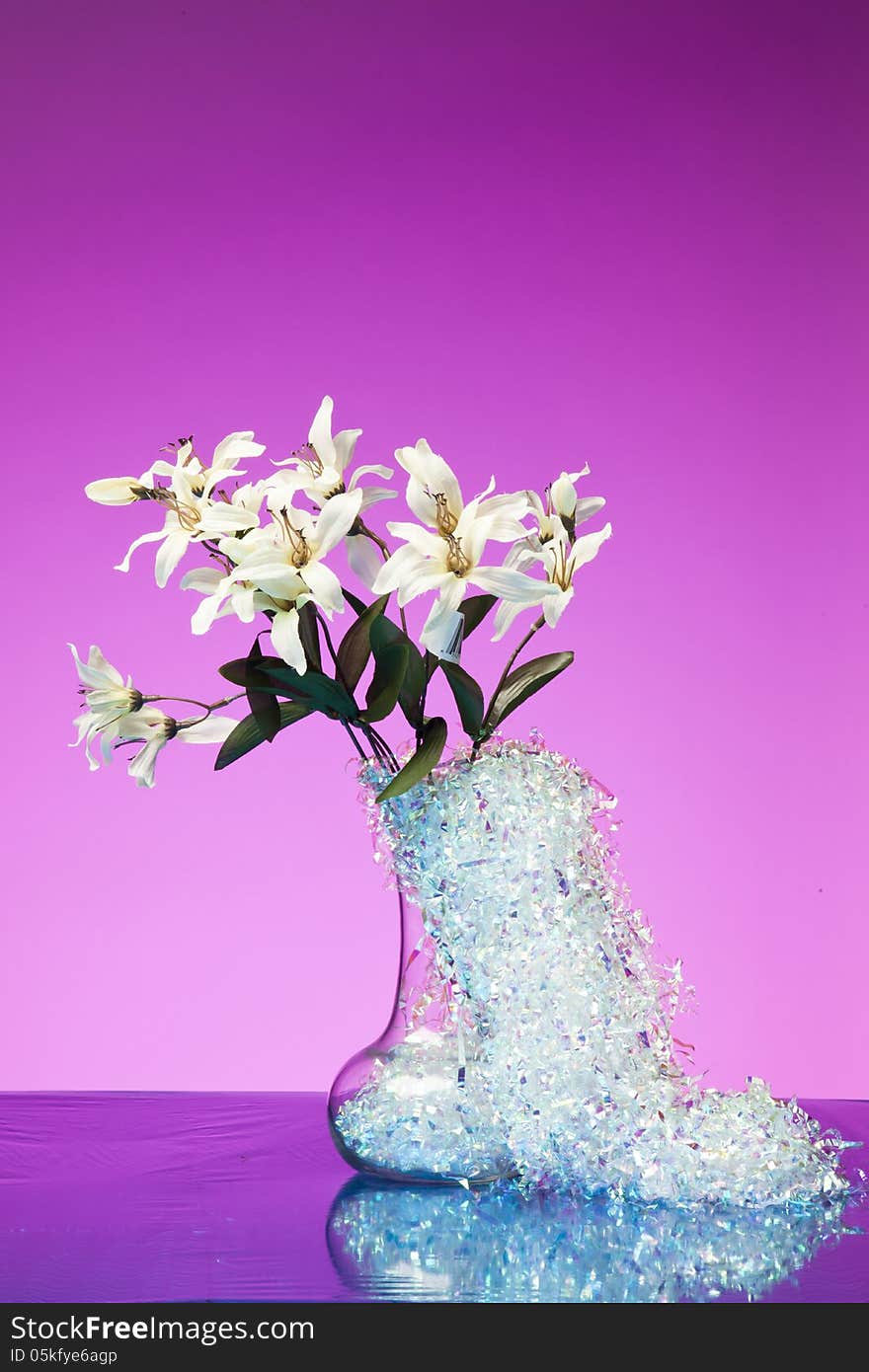 A bouquet of white flowers in a vase with silver decorative tinsel against a bright pink background. A bouquet of white flowers in a vase with silver decorative tinsel against a bright pink background.