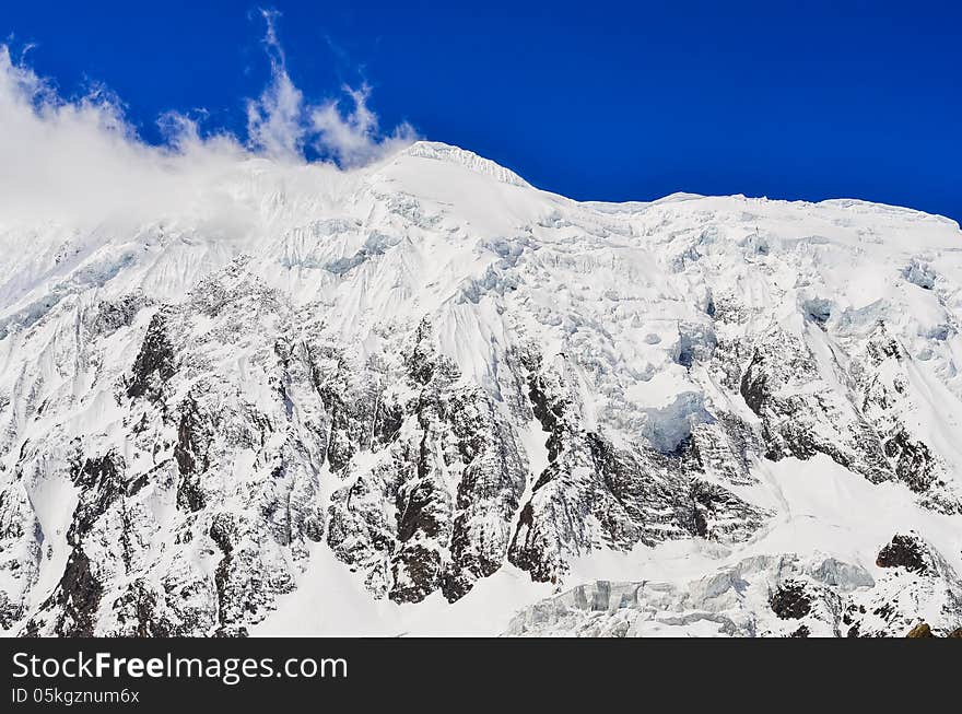 Snow mountain peak with glacier, clouds and blue sky