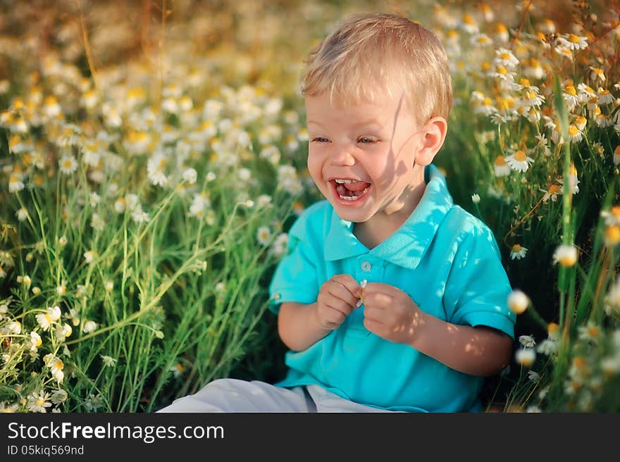 On the nature of the little baby playing and smiling on a field strewn with wild daisies. On the nature of the little baby playing and smiling on a field strewn with wild daisies