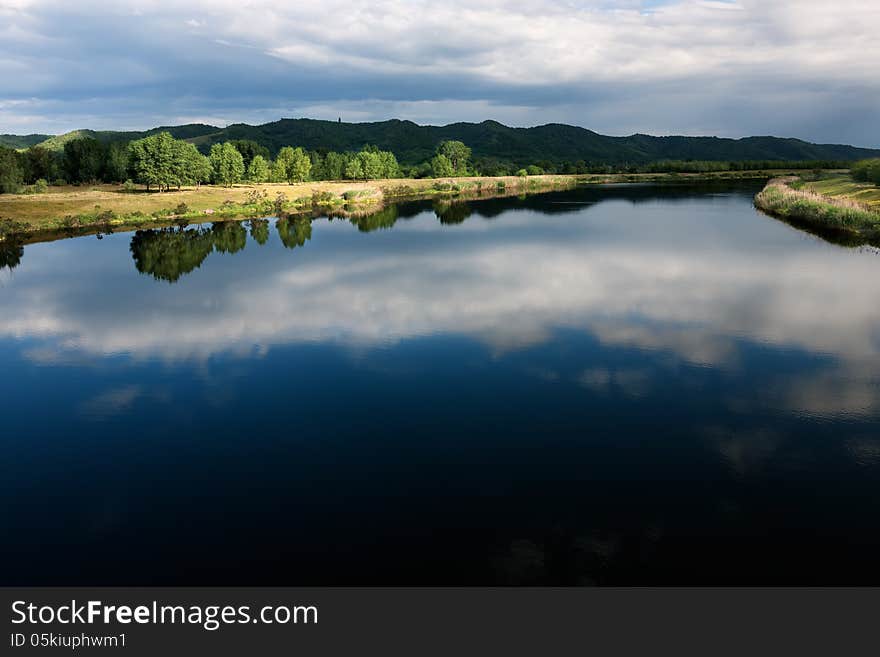 The river channel with a quiet current and clouds reflected in it. The river channel with a quiet current and clouds reflected in it.