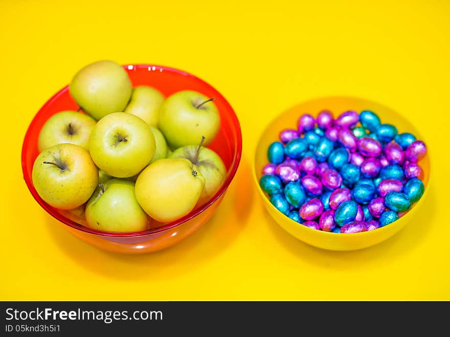 Bowls with green apples and candy on yellow background