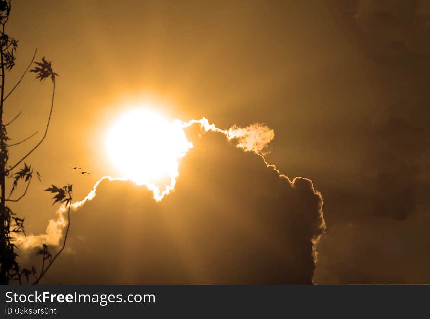 The orange sun over clouds with bright yellow sun