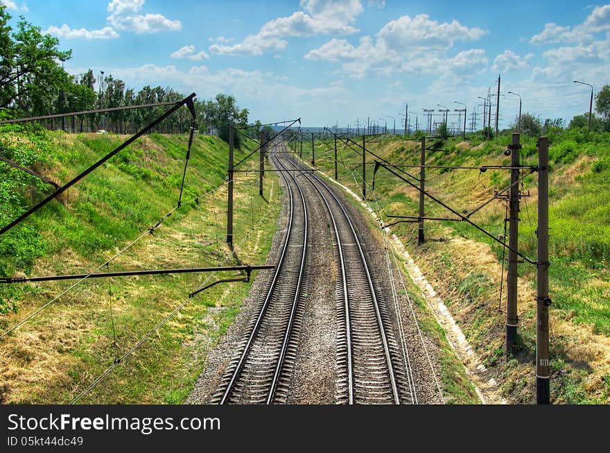 The railway leaving afar. the background of green grass and blue cloudy sky. The railway leaving afar. the background of green grass and blue cloudy sky.