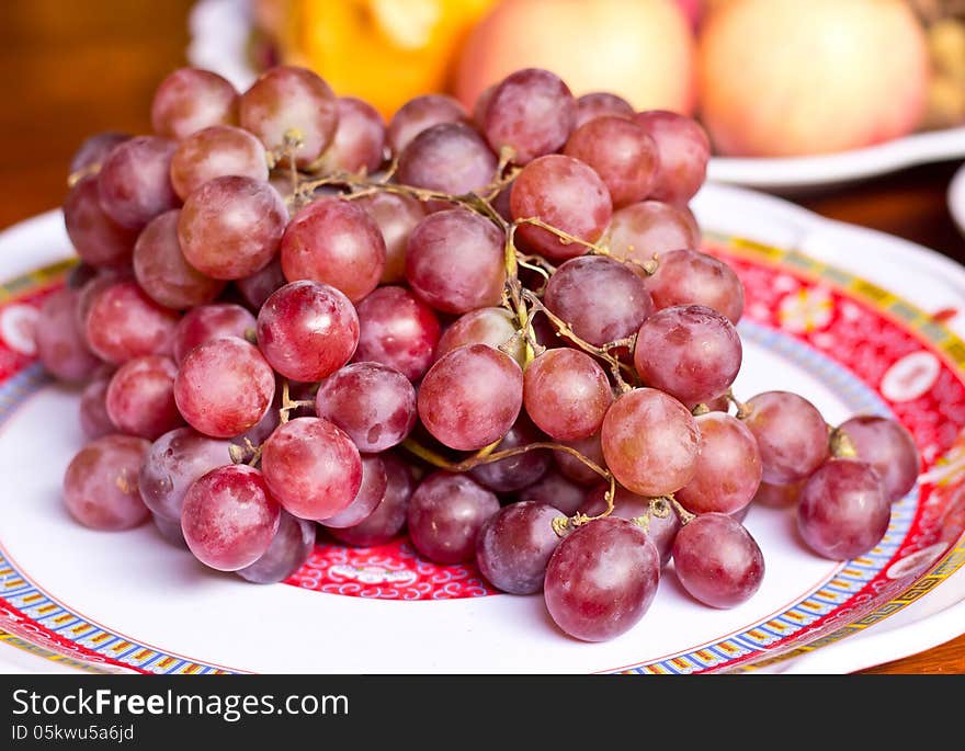 Red grape berries in white plate on straw tray closeup