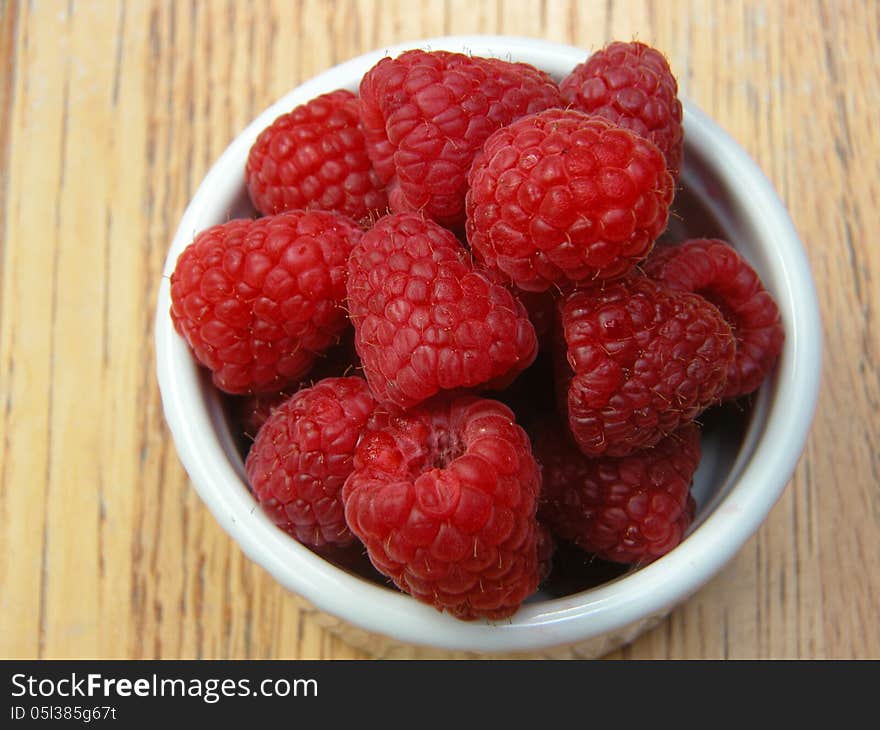 Juicy, ripe, red raspberries are displayed in a white bowl, providing one of the taste sensations of summer.