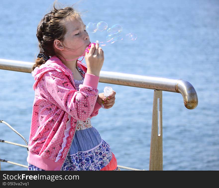 Girl with flecks blowing bubbles on sea background. Girl with flecks blowing bubbles on sea background