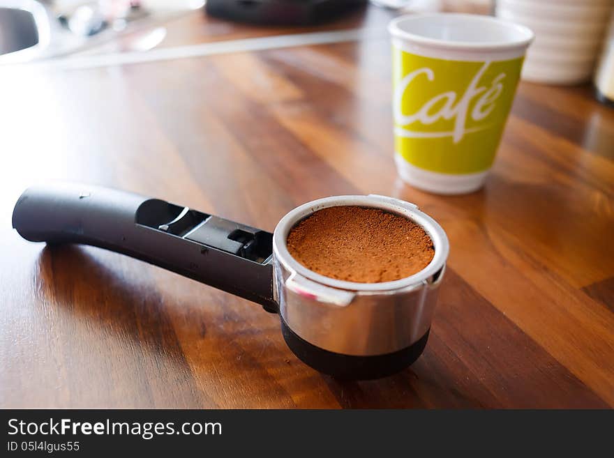 Portafilter with fresh ground coffee on kitchen worktable.