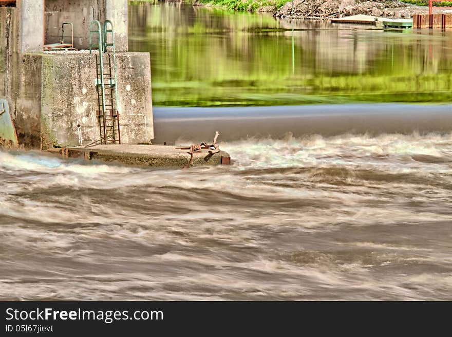 River weir with strong water current and reflections of greenery