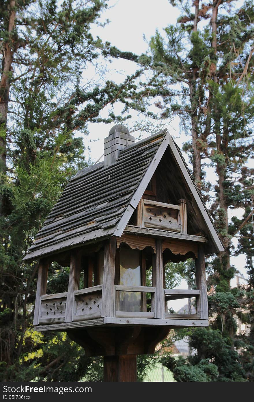 A deluxe wooden birdhouse with tall green pine trees in the background. A deluxe wooden birdhouse with tall green pine trees in the background.