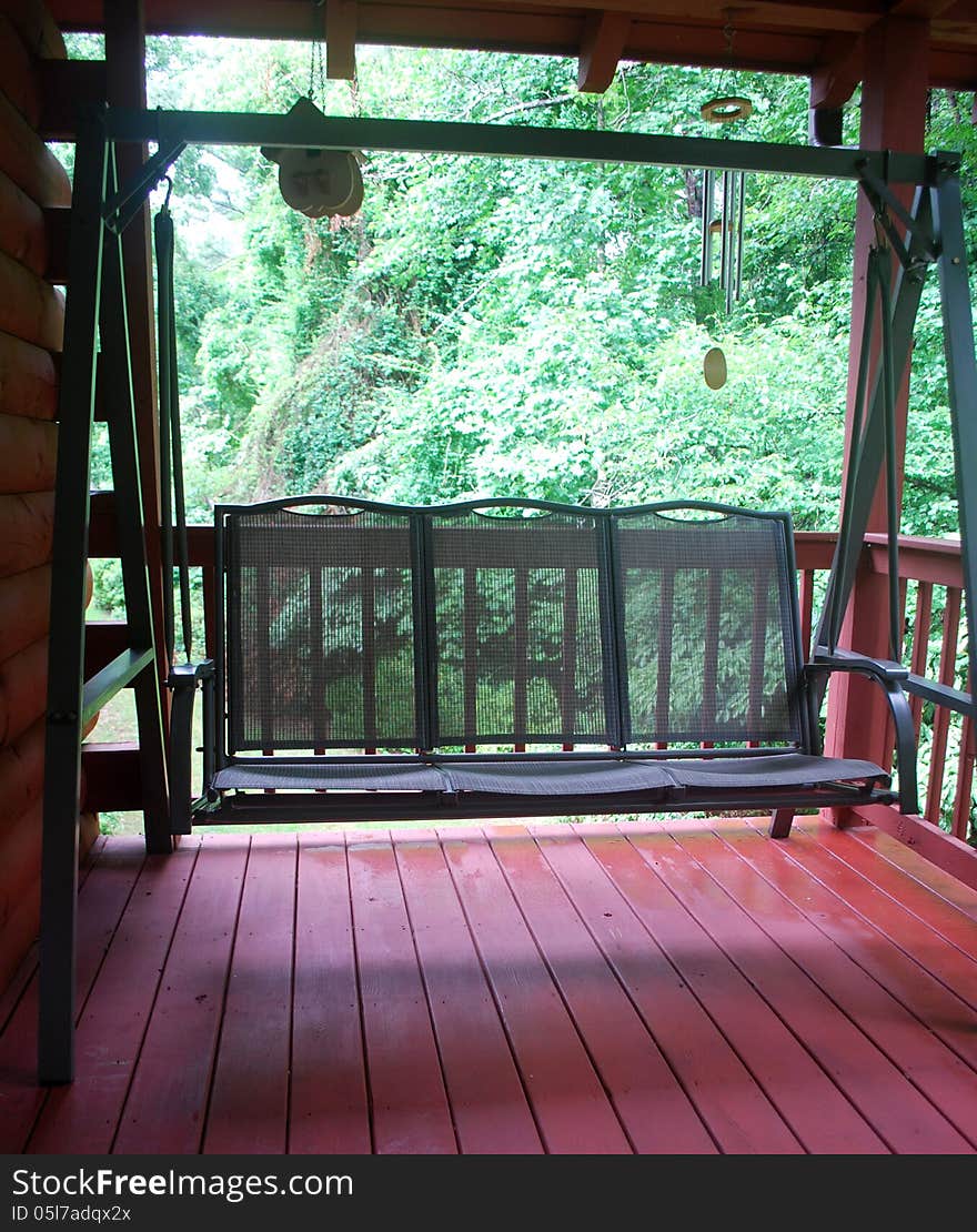 A green porch swing located on the wooden back deck of a log home in the country.